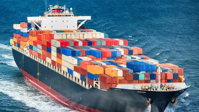 An aerial view of a large cargo ship full of colorful containers sailing across the open blue ocean.