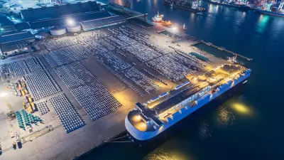 Aerial view of a cargo ship docked at a port with hundreds of vehicles lined up for export.