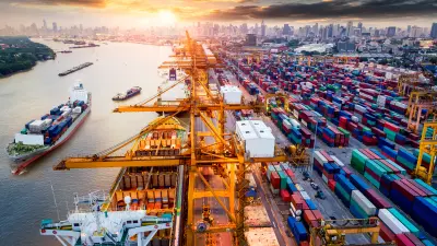 Aerial panorama of a busy shipping port with cranes, cargo ships, and stacks of colorful containers at sunset.