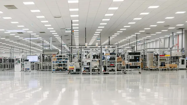 A wide shot of a large, modern, and clean factory floor with a highly reflective white surface and bright overhead lighting.