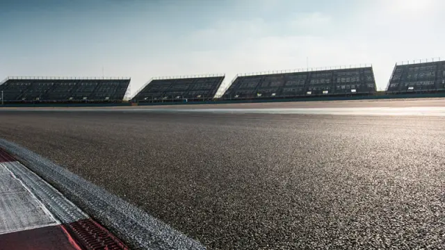 An empty racetrack and grandstands on a sunny day, viewed from the track level.