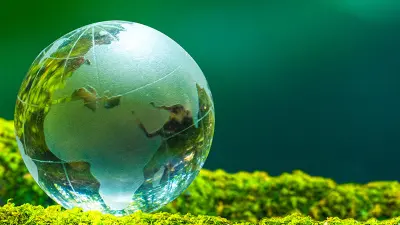 A glass globe of the Earth rests on a bed of bright green moss against a lush, out-of-focus green background.