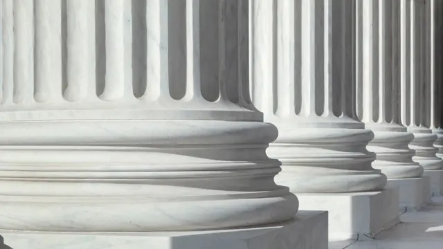 A close-up of the bases of large, white marble columns of a government or courthouse building