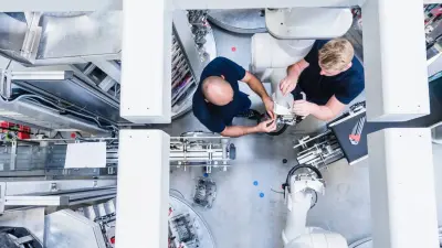 Overhead view of two engineers working together on complex robotic machinery in a factory.