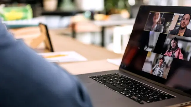 Over-the-shoulder view of a person on a laptop having a video conference call with colleagues in an office.