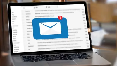 A laptop on a wooden table displays an email inbox with a large icon of a new message notification.
