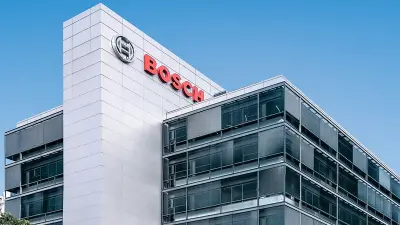 A street-level view of a modern, multi-story Bosch corporate office building with a large red logo, against a clear blue sky.