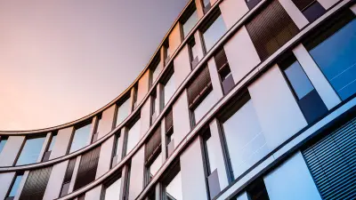 A low-angle shot of a modern, curved office building with glass windows, reflecting the colors of a sunset sky.